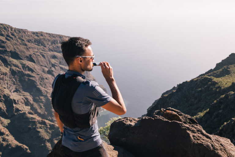 man standing on a mountain eating energy gel while looking onto the water - scan other senses