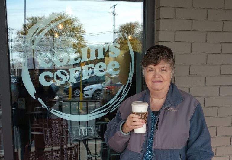 Nita Sweeney book signing - Nita standing in front of Colin's Coffee holding a cup